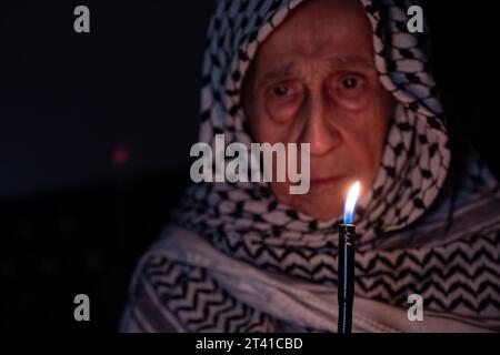 Porträt einer alten Dame, die im Dunkeln weißen palästinensischen Keffiyeh trägt und das Licht gegen die Besatzung hält Stockfoto