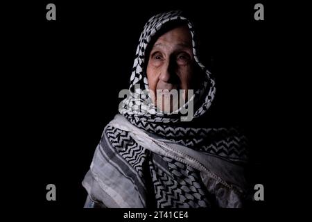 Porträt einer alten Dame in dunklem Hintergrund, die weißen palästinensischen Keffiyeh mit einem Lächeln im Gesicht trägt und nach Freiheit und Hoffnung auf das Recht auf Rückkehr sucht Stockfoto