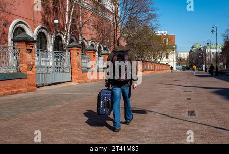 Ein Mann trägt einen blauen Koffer am Griff auf einer der Straßen im Stadtzentrum. Stockfoto