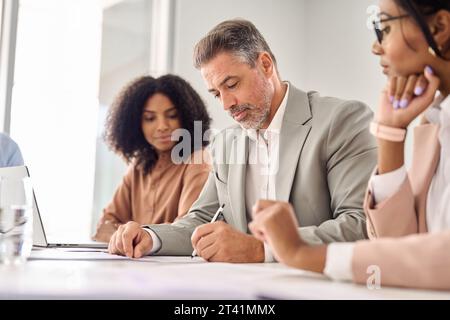Ein älterer indischer Geschäftsmann unterschreibt ein juristisches Dokument bei einem Treffen mit Beratern. Stockfoto
