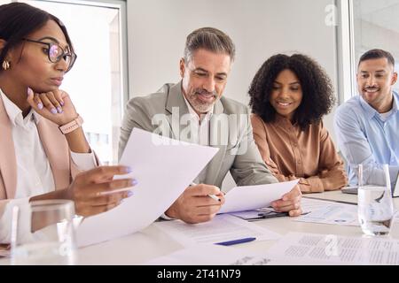Ein geschäftiger, lächelnder Geschäftsmann liest Dokumente bei der Besprechung des Büroteams. Stockfoto