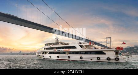 Istanbul, Türkei - 17. Mai 2023: Die weiße Fähre fährt vor Sonnenuntergang unter der Bosporus-Hängebrücke, mit der Skyline der Stadt im Hintergrund. Foto vom Beylerbeyi-Palast Stockfoto