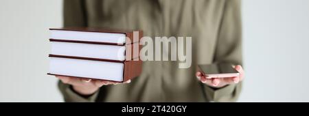Frau hält ein modernes Mobiltelefon und einen Stapel Bücher in den Händen Stockfoto