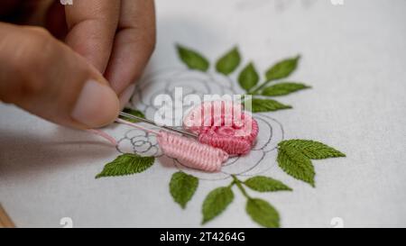 Handstickerei mit rosa Rose auf weißem Hintergrund. Stockfoto