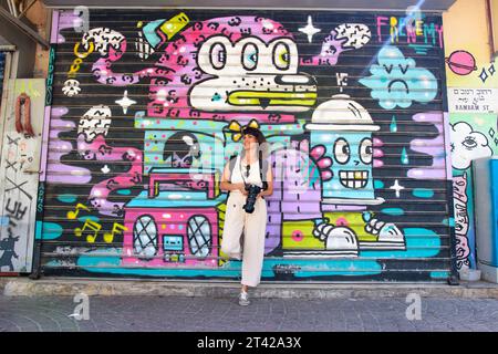 Eine junge Frau steht selbstbewusst vor einer lebendigen Wand mit Graffiti-Kunstwerken Stockfoto