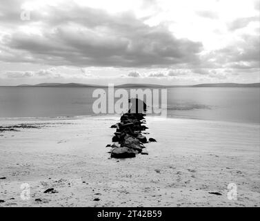 Eine ruhige Strandszene mit einem Arrangement großer, schwarzer Felsen entlang der Küste Stockfoto