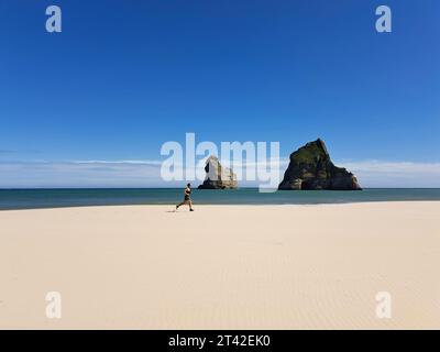Ein Mann, der an einem Sandstrand entlang läuft, mit dem blauen Meer im Hintergrund Stockfoto