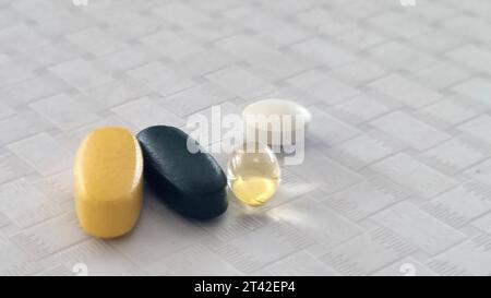 Eine weiße Flasche Kapseln und mehrere mehrfarbige Tabletten liegen auf einer flachen weißen Oberfläche Stockfoto