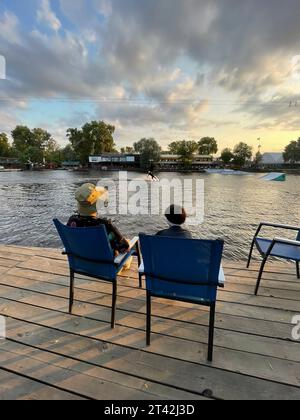 Zwei Millennials genießen einen sonnigen Tag in der freien Natur, sitzen in Liegestühlen an einem Dock an einem ruhigen See Stockfoto