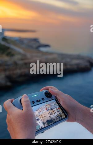 Ein Drohnenpilot bedient die Fernbedienung und manövriert die Drohne geschickt, um atemberaubende Fotos und Videos des faszinierenden italienischen Sonnenuntergangs aufzunehmen. Stockfoto