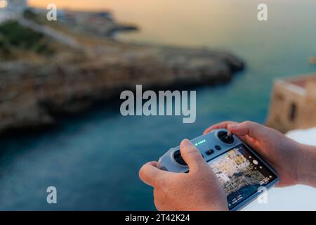 Ein Drohnenpilot bedient die Fernbedienung und manövriert die Drohne geschickt, um atemberaubende Fotos und Videos des faszinierenden italienischen Sonnenuntergangs aufzunehmen. Stockfoto