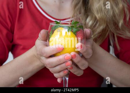 Eine Frau, die ein hohes Glas hält, gefüllt mit einer erfrischenden Mischung aus Zitronen und Himbeeren Stockfoto