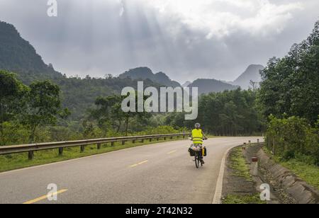 Ein männlicher Motorradfahrer fährt eine malerische Straße entlang, umgeben von üppigem Berggelände im Hintergrund Stockfoto