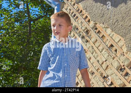 Im Sommer steht der Junge auf dem Hintergrund einer Fassade einer alten Hauswand Stockfoto