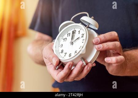 Augsburg, Bayern, Deutschland. Oktober 2023. Der alte Mann stellt die Uhr auf einen Wecker von der Sommerzeit auf die Winterzeit zurück. Uhrenwechselkonzept *** Alter Mann stellt die Uhr an einem Wecker von Sommerzeit zurück auf Winterzeit. Uhrumstellung Konzept Credit: Imago/Alamy Live News Stockfoto