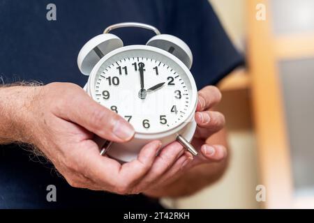 Augsburg, Bayern, Deutschland. Oktober 2023. Der alte Mann stellt die Uhr auf einen Wecker von der Sommerzeit auf die Winterzeit zurück. Uhrenwechselkonzept *** Alter Mann stellt die Uhr an einem Wecker von Sommerzeit zurück auf Winterzeit. Uhrumstellung Konzept Credit: Imago/Alamy Live News Stockfoto