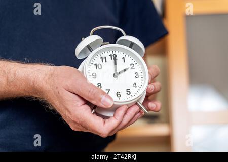 Augsburg, Bayern, Deutschland. Oktober 2023. Der alte Mann stellt die Uhr auf einen Wecker von der Sommerzeit auf die Winterzeit zurück. Uhrenwechselkonzept *** Alter Mann stellt die Uhr an einem Wecker von Sommerzeit zurück auf Winterzeit. Uhrumstellung Konzept Credit: Imago/Alamy Live News Stockfoto