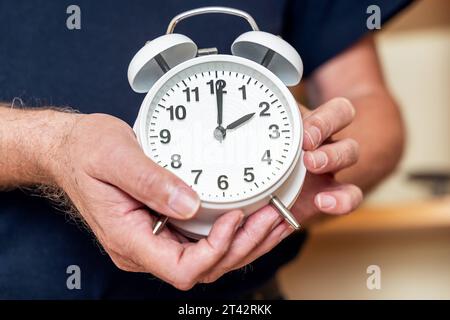 Augsburg, Bayern, Deutschland. Oktober 2023. Der alte Mann stellt die Uhr auf einen Wecker von der Sommerzeit auf die Winterzeit zurück. Uhrenwechselkonzept *** Alter Mann stellt die Uhr an einem Wecker von Sommerzeit zurück auf Winterzeit. Uhrumstellung Konzept Credit: Imago/Alamy Live News Stockfoto