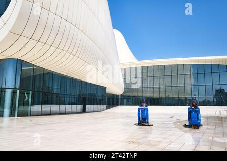 Ansicht der vorderen Fassade mit zwei Reinigungsmaschinen, die die Oberfläche reinigen. Im Heydar Aliyev Centre Arts Performance Hall in Baku, Aserbaidschan. Stockfoto