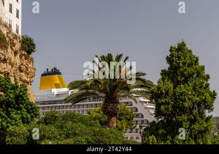 Ein sehr großes Kreuzfahrtschiff legt in Mahon auf Menorca an. Palmen tragen zur Atmosphäre dieser schönen spanischen Insel bei. Stockfoto