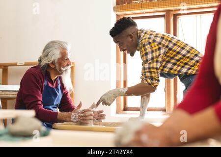 Zwei verschiedene männliche Töpfer benutzen Töpferrad und diskutieren in Töpferstudio Stockfoto