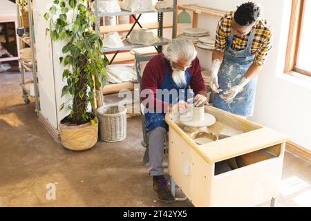 Zwei verschiedene männliche Töpfer benutzen Töpferrad und diskutieren in Töpferstudio Stockfoto