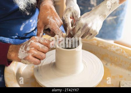 Hände von zwei verschiedenen männlichen Töpfern, die mit Töpferrad im Töpferstudio an Tonvase arbeiten Stockfoto