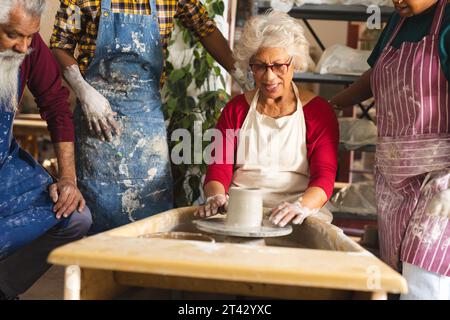 Glückliche birassische ältere Töpferin mit anderen, die Töpferrad im Töpferstudio benutzt Stockfoto