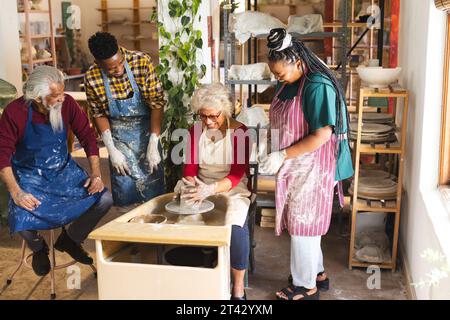 Glückliche birassische ältere Töpferin mit anderen, die Töpferrad im Töpferstudio benutzt Stockfoto