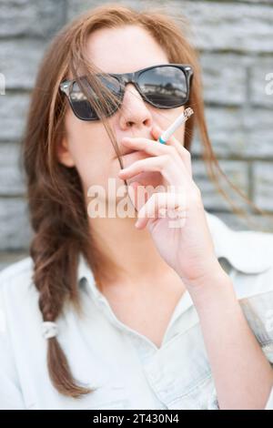 Cool, Stadt und eine Frau mit Sonnenbrille raucht mit Streetwear, stilvoll und urbaner Kultur. Mode, jung und ein Mädchen mit Rauch, Zigarette oder Stockfoto