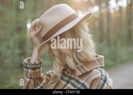 Porträt einer stilvollen jungen Frau, die in einem Wald steht, mit der Hand auf dem Hut, Weißrussland Stockfoto