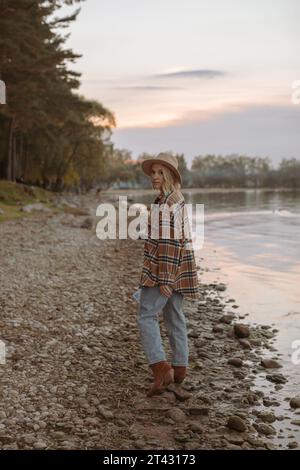 Stilvolle Frau in einer karierten Jacke mit einer Karte, die bei Sonnenuntergang an einem See steht, Weißrussland Stockfoto