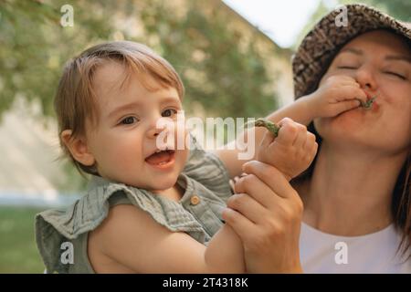 Mutter hält ihre Tochter, die ihr ein Blatt in den Mund steckt, Weißrussland Stockfoto