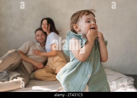 Glückliche Eltern sitzen auf dem Boden in einem Wohnzimmer und beobachten ihre Tochter beim Spielen Stockfoto