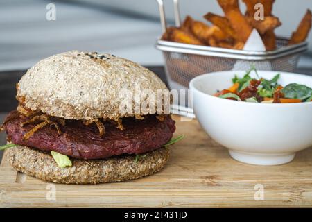 Nahaufnahme eines Rote-Bete-Bohnen-Burgers mit gebratenen Zwiebeln, Süßkartoffelfritten, Salat und Dippsoße Stockfoto