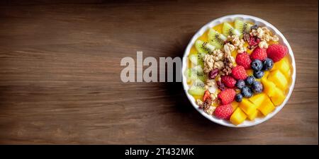 Gesunder Mango-Frucht-Smoothie mit Heidelbeeren, Himbeeren, Kiwi und Müsli. Draufsicht auf braunem Holzhintergrund. Stockfoto