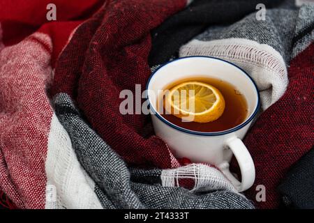 Nahaufnahme einer Tasse heißem schwarzen Tee mit Zitrone in einen Schal gewickelt Stockfoto
