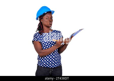 Porträt einer schönen jungen Bauingenieurin, die einen Schutzhelm trägt und in eine Zwischenablage schreibt. Stockfoto