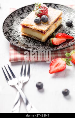 Ein Stück Napoleonkuchen mit Mohnsamen und Kirschen, dekoriert mit Erdbeeren und Blaubeeren auf hellem Hintergrund. Schließen Stockfoto