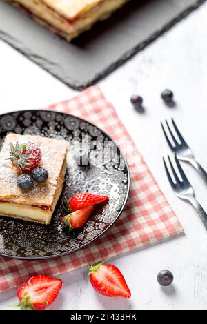 Ein Stück Napoleonkuchen mit Mohnsamen und Kirschen, dekoriert mit Erdbeeren und Blaubeeren auf hellem Hintergrund. Schließen Stockfoto