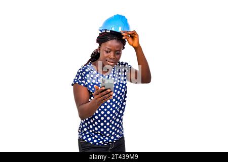 Eine schöne Ingenieurin mit Sicherheitshelm, der über weißem Hintergrund steht und das Handy mit überraschtem Blick betrachtet. Stockfoto