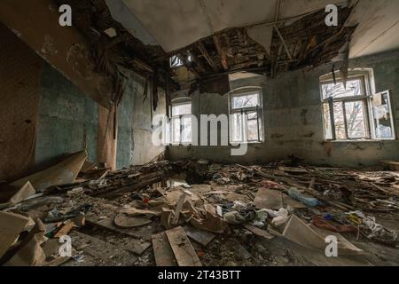 Von oben aus der geräumigen Halle mit Glasfenstern und Schutthaufen mit beschädigten Möbeln auf dem Boden mit Loch während zerstörter Dekoration Stockfoto