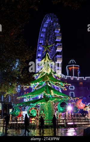 Perpignans bezaubernde Weihnachtsszene: Ein glitzernder Baum und ein beleuchtetes Riesenrad schaffen ein faszinierendes Urlaubsambiente unter dem Nachthimmel. Stockfoto