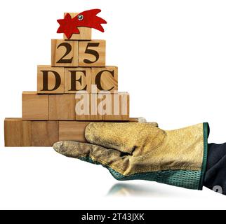 Hand mit Arbeitshandschuhen, die einen kleinen hölzernen Weihnachtsbaum halten, der aus kleinen Holzwürfeln mit einem roten Kometenstern und Text vom 25. Dezember besteht, isolieren Stockfoto