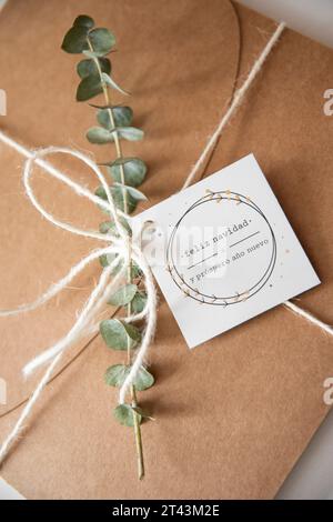 Ein festlicher Hauch von rustikalem Charme: Geschenkbox aus Papier mit Eukalyptus und einer „Merry Christmas“-Karte, perfekt für herzliche Weihnachtsgeschenke. Stockfoto