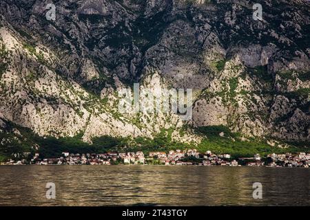 Kleinstädte liegen unter senkrechten Felswänden und umarmen die Küste in der Bucht von Kotor entlang der Adriaküste Montenegros. Stockfoto