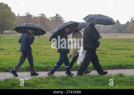 Wimbledon, London, Großbritannien. 28. Oktober 2023. Leute, die mit Sonnenschirmen auf dem Wimbledon Common während der Regenschauer auf dem Wimbledon Common, Südwesten Londons, herumlaufen. Das Met Office hat einen Hochwasseralarm ausgegeben, da starke Regenfälle, 70 km/h Wind in Südengland und Schottland dieses Wochenende treffen werden. Credit amer Gazzal/Alamy Live News Stockfoto