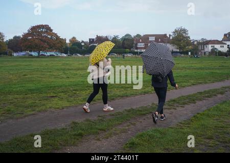 Wimbledon, London, Großbritannien. 28. Oktober 2023. Leute, die mit Sonnenschirmen im Wimbledon Common im Wimbledon Common im Südwesten Londons Schutz bieten. Während Regenschauer hat das Met Office Hochwasseralarm ausgegeben, da starke Regenschauer, 70 km/h Wind in Südengland und Schottland dieses Wochenende treffen werden. Credit amer Gazzal/Alamy Live News Stockfoto