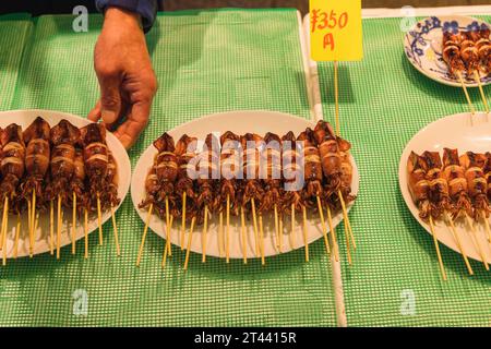 Calamari-Spieße, die auf Tellern für die Präsentation eines Straßenktichen von männlicher Hand in einer Straßenküche in Tokio, Japan, serviert wurden Stockfoto