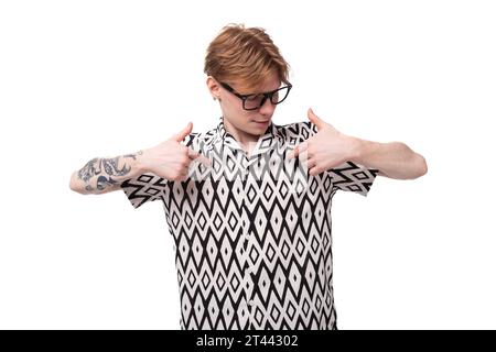 Nahaufnahme eines jungen rothaarigen Mannes in Brille mit einem Tattoo am Arm, der sein schwarz-weißes Sommerhemd zeigt Stockfoto